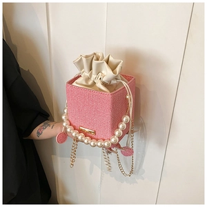 Pink woven bucket bag featuring elegant faux pearl handle and gold chain strap detail