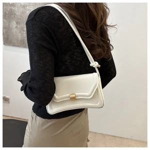 Detail of minimalist cream saddle bag featuring a matte gold square buckle and leather texture