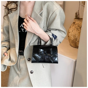 Detailed view of women's black glossy patent leather handbag with a large bow and ruffled texture