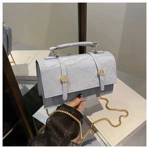 Detail of light blue textured handbag with gold chain strap and buckle closure