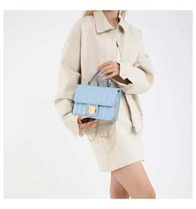 Detail of light blue square crossbody bag featuring vertical quilted texture and gold lock