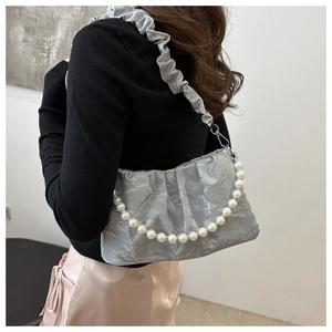 Borsa baguette plissettata argento con catena di perle indossata come borsa sottobraccio