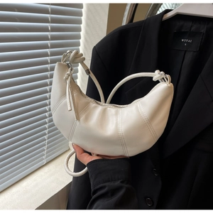 Detail of white croissant bag featuring vertical stitching and a distinctive knotted strap