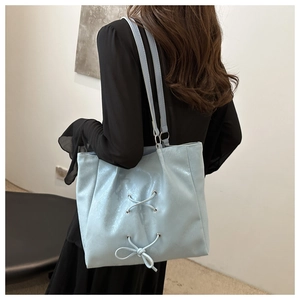 Detail of light blue glossy tote bag featuring a decorative ribbon bow and slim shoulder straps