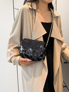 Fashionable black sequin crossbody bag with silver chain strap worn with casual trench coat