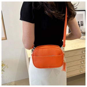 Dettaglio della borsa a tracolla arancione con texture in pelle martellata e nappa in pelle