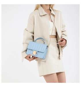Close-up of light blue crossbody bag featuring gold clasp and vertical quilted texture
