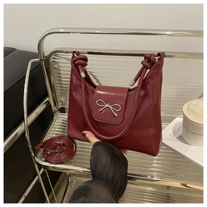 Détail du sac en cuir verni rouge foncé avec nœud argenté et poignée nouée