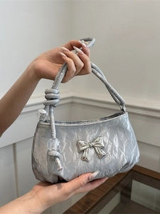 Silver metallic wrinkled handbag with bow detail and knotted handle shown in hand