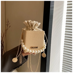 Detail of woven square bag featuring pearl handle and gold chain in soft window light