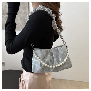 Detail of silver pleated cloud bag featuring glossy satin finish and pearl chain ornament