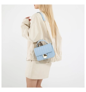 Detail of light blue quilted crossbody bag with golden chain strap on shoulder