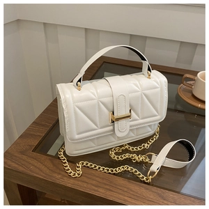Detail of white quilted handbag with golden chain strap on an elegant glass surface