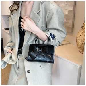 Detail of elegant black glossy handbag featuring a prominent bow design and sleek texture