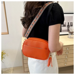 Close-up of orange lychee leather camera bag with colorful geometric woven strap
