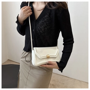 Close-up of a white glossy saddle bag with gold metal buckle on a fashion model
