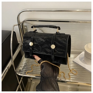 Detail of black wrinkled texture bag featuring gold buttons and metallic chain strap