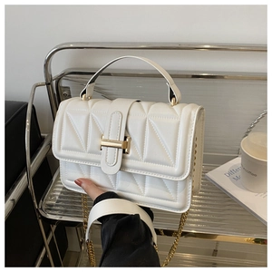 Detail of white textured square bag with golden H clasp and quilted stitching