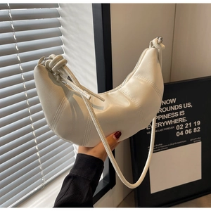 Detail of white croissant bag featuring vertical stitching and a stylish knotted shoulder strap