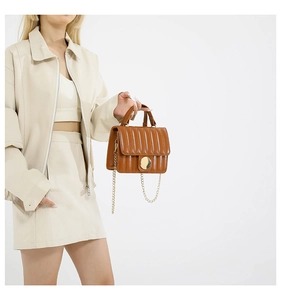 Close-up of caramel brown quilted handbag with gold chain strap and metal buckle detail