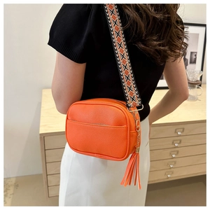 Close-up of orange lychee leather crossbody bag with ethnic geometric wide strap and tassel