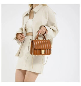 Brown quilted handbag with gold oval lock and chain strap carried by a model