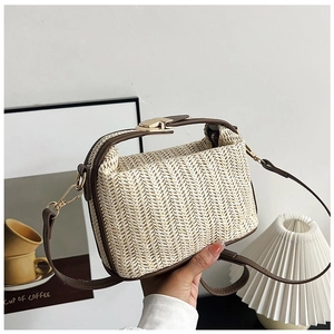 Close-up of woven straw shoulder bag featuring brown leather trim and golden clasp buckle