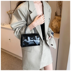 Close-up of a glossy black bow handbag with crinkle leather texture and elegant top handle