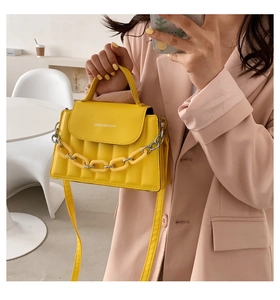 Macro detail of yellow quilted PU leather bag with decorative chain and adjustable strap