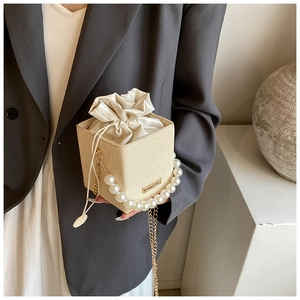 Close-up of beige woven bucket bag with elegant pearl handle and gold chain detail