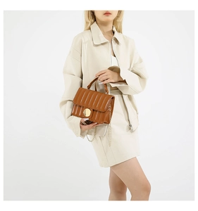 Detail of caramel brown quilted bag with gold circular buckle and chain strap on model