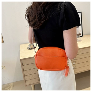 Detailed back view of orange textured crossbody bag with geometric woven shoulder strap