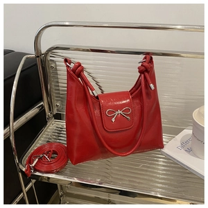 Détail du sac bandoulière en cuir rouge brillant avec nœud métallique argenté et sangle