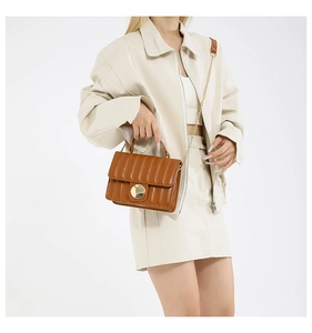 Detail of a brown quilted crossbody bag with golden metal lock and vertical stripes