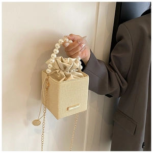 Detail view of woven straw bucket bag featuring pearl handle and golden chain strap