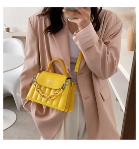 Detail of yellow quilted crossbody bag with a chunky chain strap on a pink blazer