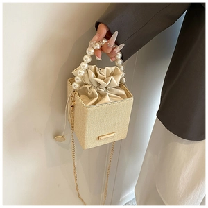 Close-up of beige woven bucket bag with large faux pearl handle and gold chain strap