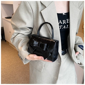 Close-up of black glossy patent leather handbag with large bow detail held by model