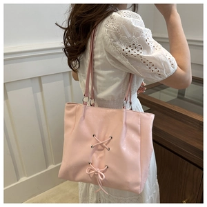 Close-up of pink tote bag with bow detail and silver rings on model's shoulder