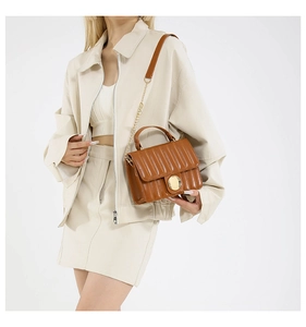 Detailed view of brown quilted bag with gold chain strap and circular metal lock closure