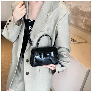 Detailed view of black glossy patent leather crossbody bag with bow decoration and handle