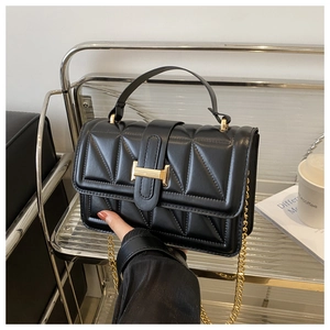 Close-up of black quilted handbag featuring a gold H-buckle and elegant chain strap