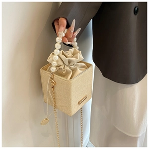 Détail du sac seau tissé beige avec poignée en perles et bandoulière dorée