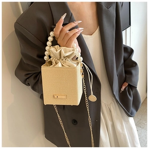 Detail of beige woven bucket bag featuring pearl handle and satin drawstring lining