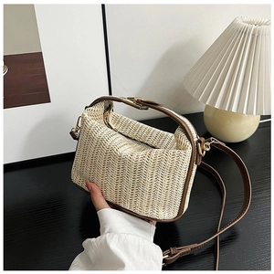 Close-up of woven straw handbag with brown leather trim and golden hardware details