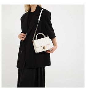 Detail of white quilted handbag with gold metal lock and chain strap on a black blazer
