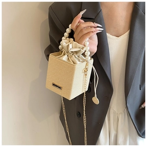 Detail of a chic cream textured mini bucket bag with pearl handle and gold chain strap