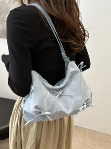 Light blue pleated shoulder bag with bow accents worn by model in a minimalist setting