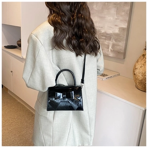 Chic black patent leather handbag featuring a large bow detail shown on a model