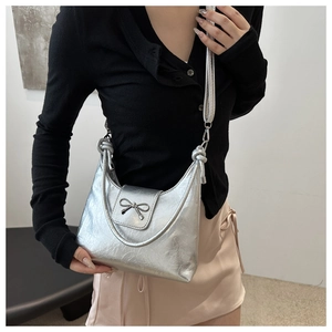 Silver metallic bucket bag with bow detail and knotted shoulder strap in minimalist setting